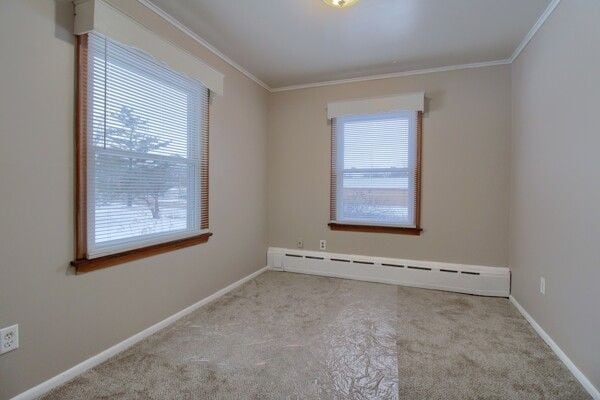 empty room with a baseboard heating unit, light colored carpet, and crown molding