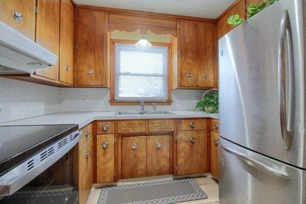 kitchen featuring sink, stainless steel refrigerator, light tile patterned floors, and range with electric stovetop