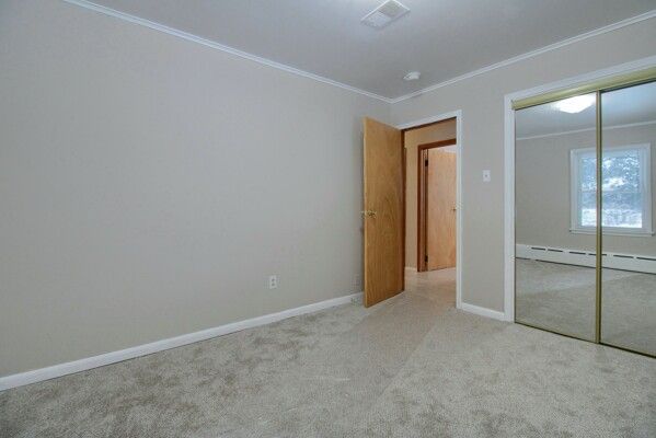 unfurnished bedroom with a closet, light carpet, ornamental molding, and baseboard heating