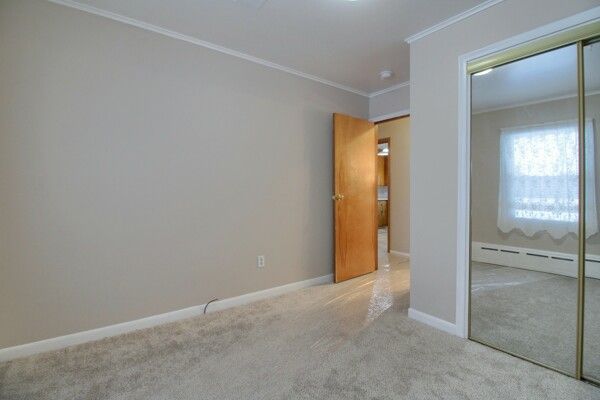 unfurnished bedroom with ornamental molding, baseboard heating, and light carpet