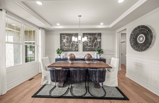 dining area featuring a raised ceiling, a notable chandelier, and light wood-type flooring