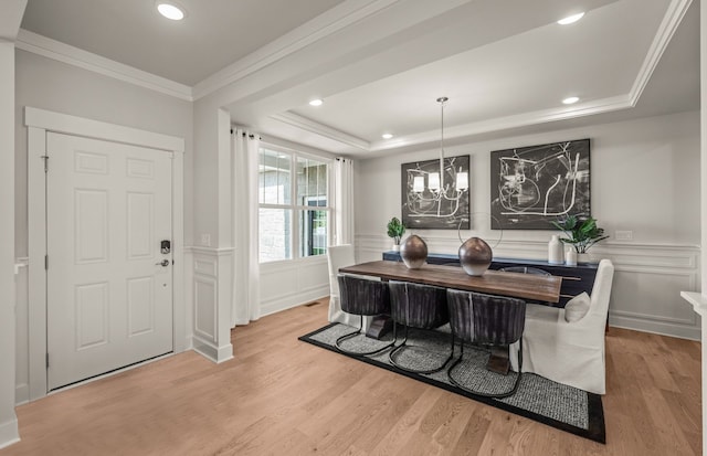 dining area with a raised ceiling, a chandelier, ornamental molding, and light wood-type flooring