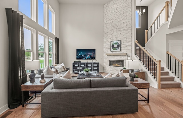 living room with light wood-type flooring, a fireplace, a towering ceiling, and a chandelier