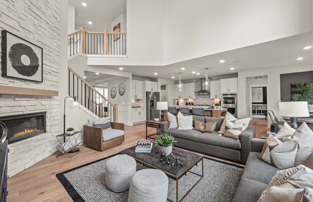 living room featuring a stone fireplace, a towering ceiling, and light wood-type flooring