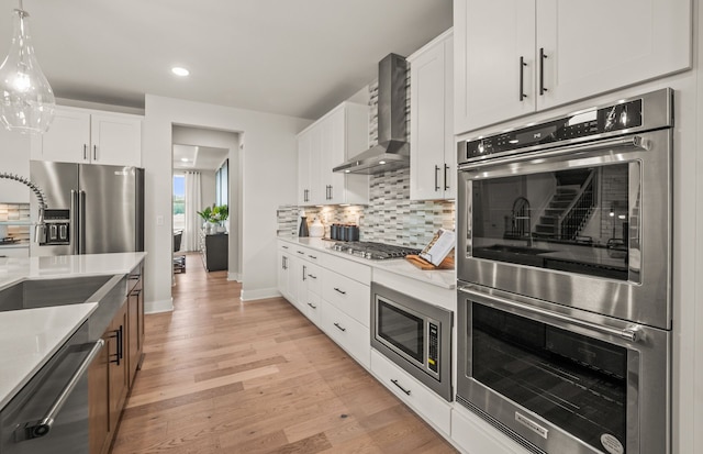 kitchen featuring white cabinetry, hanging light fixtures, wall chimney range hood, decorative backsplash, and appliances with stainless steel finishes