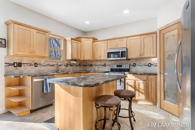 kitchen featuring sink, light brown cabinets, stainless steel appliances, dark stone countertops, and a kitchen island