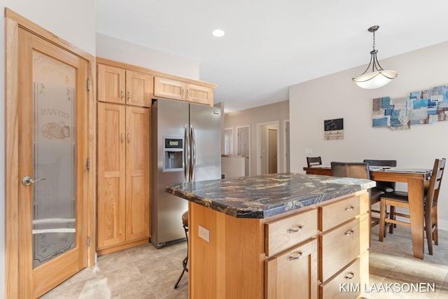 kitchen with stainless steel fridge, light brown cabinetry, pendant lighting, dark stone countertops, and a kitchen island