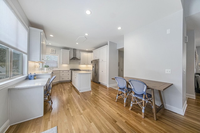 kitchen with a kitchen bar, high end fridge, wall chimney exhaust hood, white cabinets, and a center island