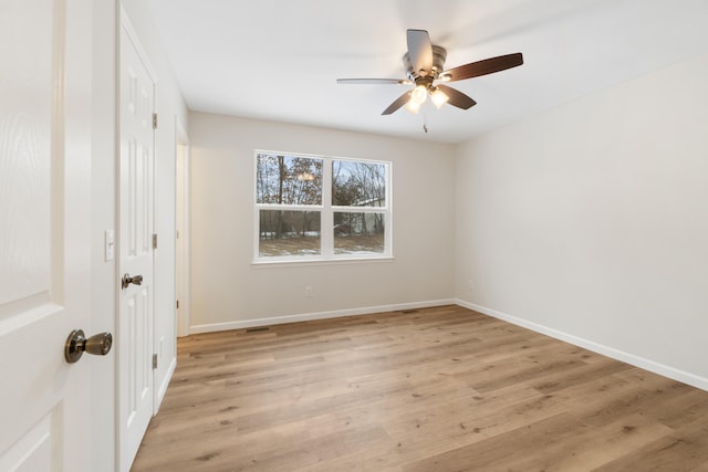 spare room featuring light wood finished floors, a ceiling fan, and baseboards