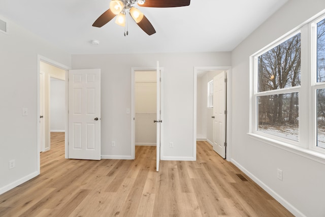 unfurnished bedroom featuring ceiling fan, light wood-type flooring, a walk in closet, and a closet