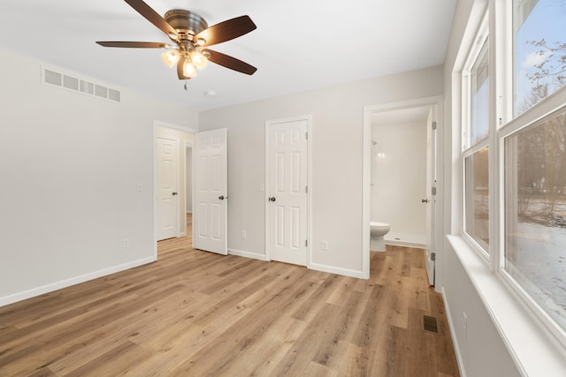 unfurnished bedroom featuring ensuite bathroom, ceiling fan, light hardwood / wood-style floors, and multiple windows