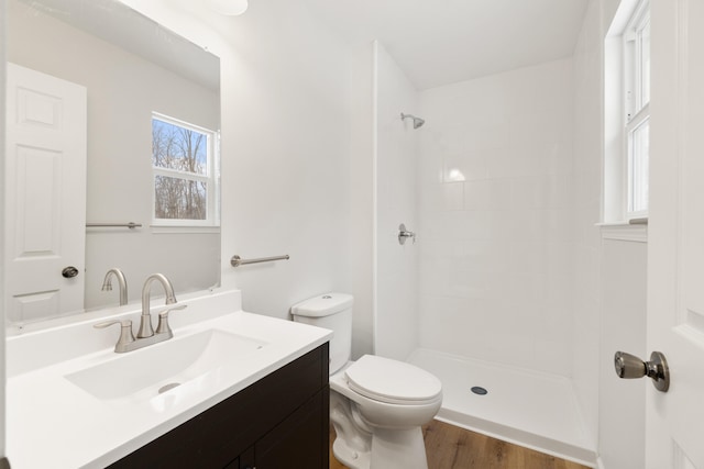 bathroom with a tile shower, vanity, toilet, and wood finished floors