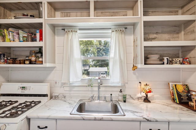 kitchen with white range with gas cooktop, wood walls, light stone counters, and sink