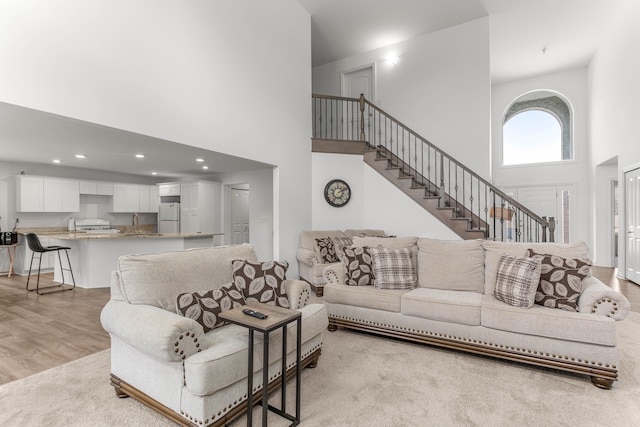 living room featuring light wood-type flooring, sink, and a high ceiling