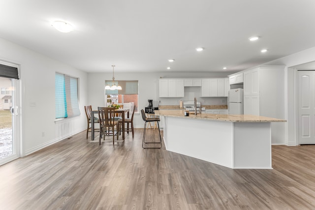 kitchen featuring pendant lighting, a center island with sink, white cabinets, white refrigerator, and light stone counters