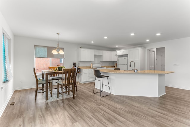 kitchen with pendant lighting, white refrigerator, a center island with sink, range, and white cabinetry