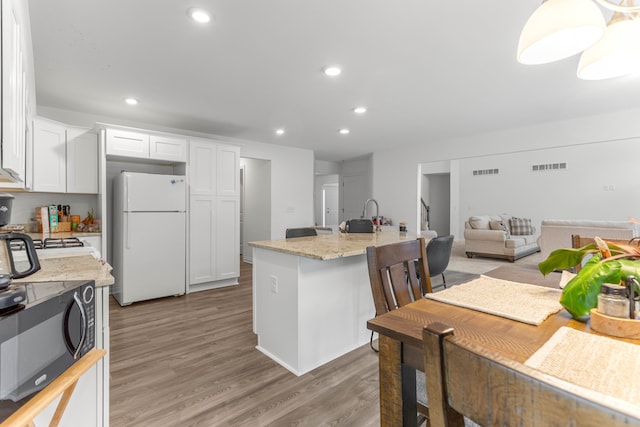 kitchen featuring light stone countertops, an island with sink, light wood-type flooring, white fridge, and white cabinetry