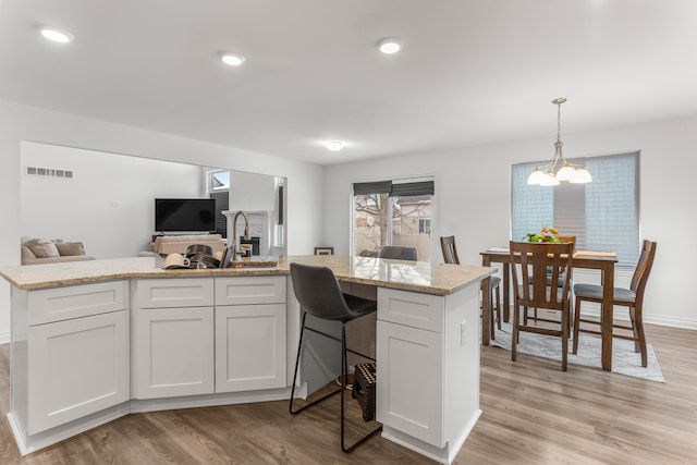 kitchen with pendant lighting, an inviting chandelier, white cabinetry, and light hardwood / wood-style floors