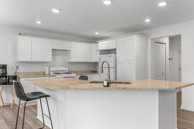 kitchen with white cabinetry, light stone countertops, an island with sink, white appliances, and a breakfast bar