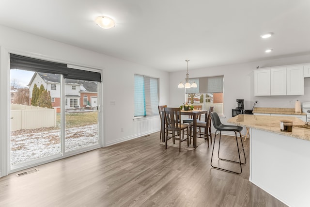 kitchen with white cabinetry, light stone countertops, decorative light fixtures, a breakfast bar area, and hardwood / wood-style flooring