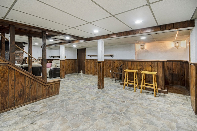 basement featuring a paneled ceiling, wood walls, and bar