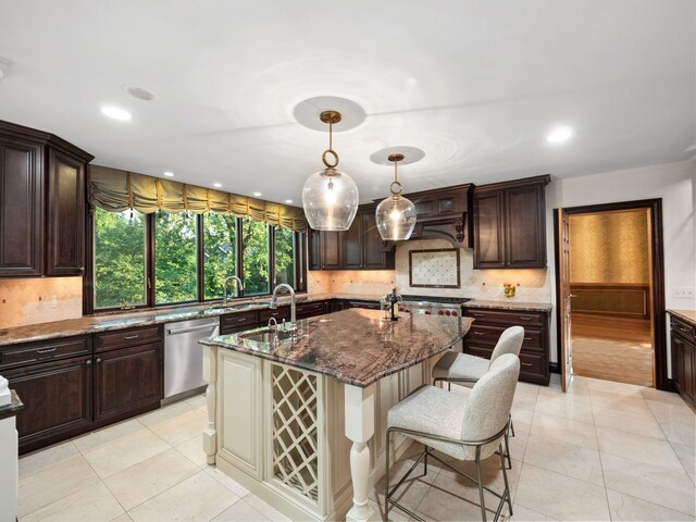 kitchen with sink, dark stone countertops, stainless steel dishwasher, hanging light fixtures, and a kitchen island with sink