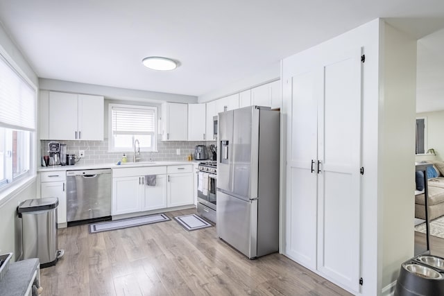 kitchen featuring appliances with stainless steel finishes, light wood-type flooring, sink, white cabinetry, and backsplash