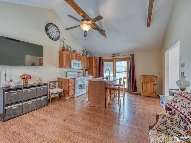 kitchen with high vaulted ceiling, an island with sink, white appliances, a breakfast bar, and light wood-type flooring