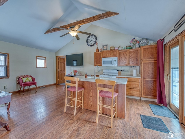 kitchen with vaulted ceiling with beams, an island with sink, light hardwood / wood-style floors, white appliances, and a breakfast bar area