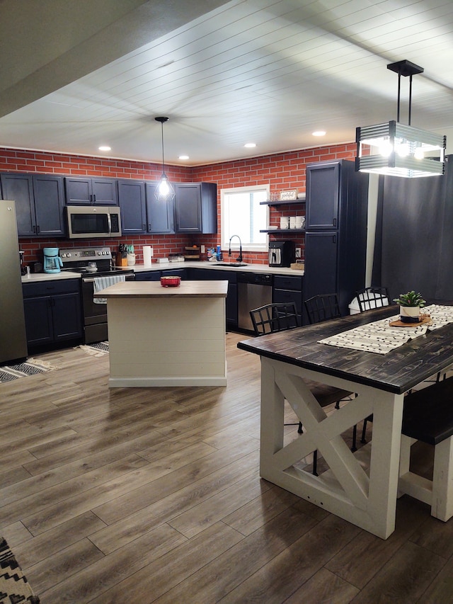 kitchen with hardwood / wood-style floors, a center island, sink, hanging light fixtures, and stainless steel appliances