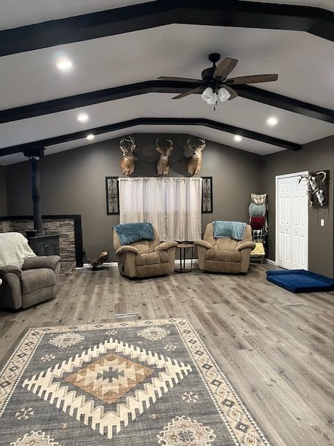 interior space with a wood stove, ceiling fan, lofted ceiling with beams, and wood-type flooring