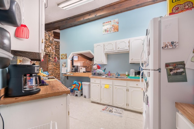 kitchen featuring white cabinets, white refrigerator, sink, butcher block countertops, and beam ceiling