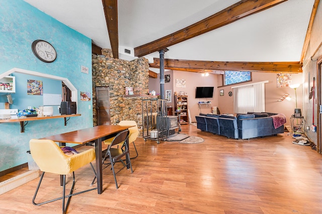 dining room with beam ceiling, a wood stove, a towering ceiling, and light hardwood / wood-style floors