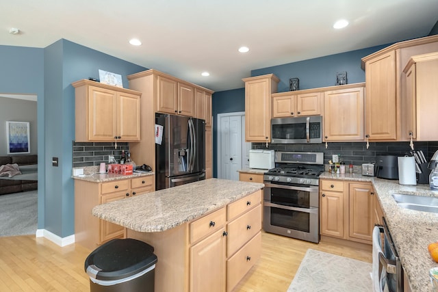 kitchen featuring light brown cabinetry, backsplash, stainless steel appliances, light hardwood / wood-style flooring, and a center island