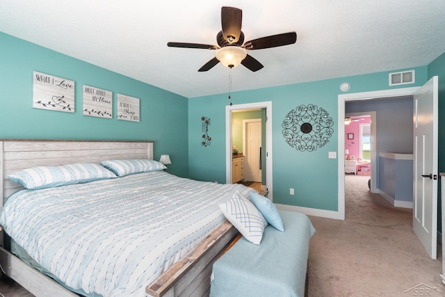 bedroom featuring ceiling fan, ensuite bathroom, light carpet, and a textured ceiling