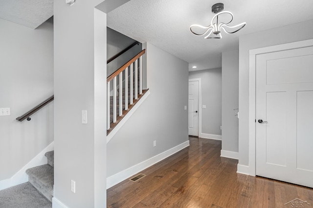 staircase with baseboards, visible vents, hardwood / wood-style flooring, an inviting chandelier, and a textured ceiling