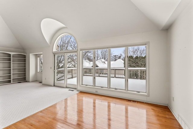 spare room with built in shelves, light colored carpet, and vaulted ceiling