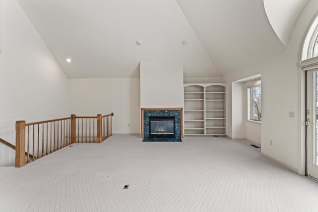 carpeted living room featuring built in shelves, lofted ceiling, and a premium fireplace