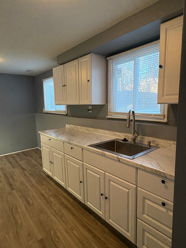 kitchen with white cabinets, dark hardwood / wood-style floors, light stone counters, and sink