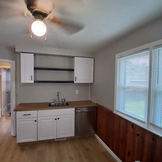 kitchen with sink, light hardwood / wood-style flooring, stainless steel dishwasher, wood walls, and white cabinets