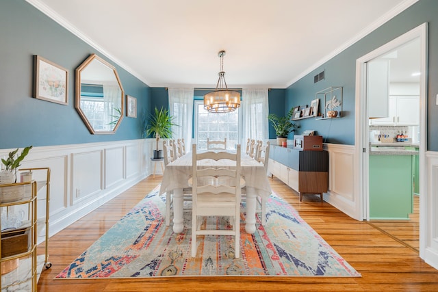 dining area with light wood-type flooring, an inviting chandelier, and ornamental molding