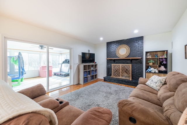 living room featuring light wood-type flooring, a brick fireplace, and ceiling fan