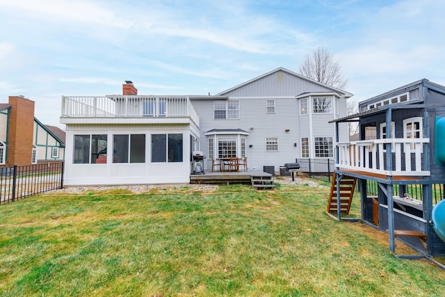 back of property with a yard, a playground, a wooden deck, and a sunroom