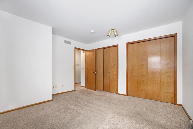 unfurnished bedroom featuring light colored carpet and two closets