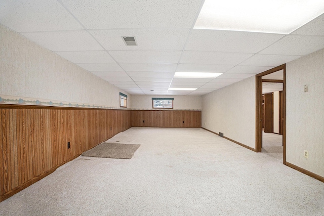 basement featuring light colored carpet, a drop ceiling, and wooden walls