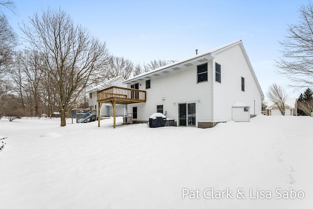 snow covered house with central air condition unit and a wooden deck