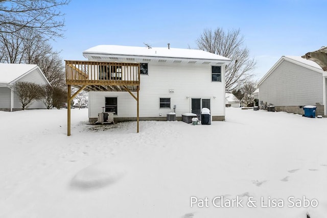 snow covered back of property with a wooden deck and central AC