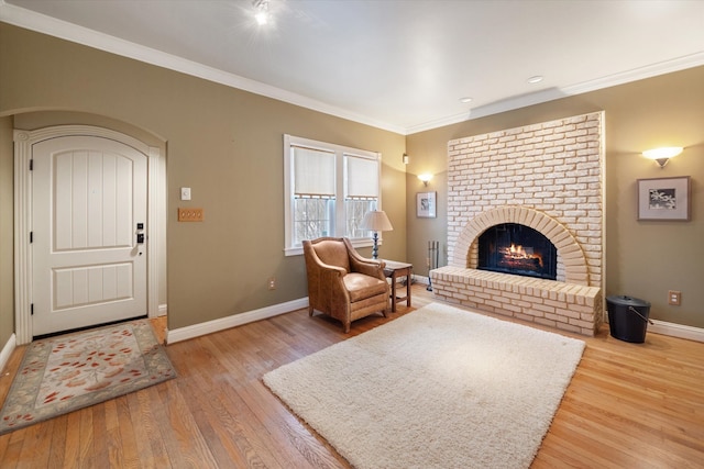 living room featuring a brick fireplace, ornamental molding, and light wood-type flooring