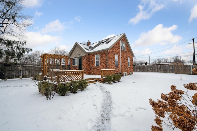 snow covered back of property with a pergola