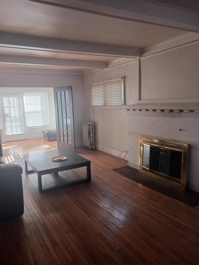 living room with beamed ceiling, wood-type flooring, radiator heating unit, and a brick fireplace